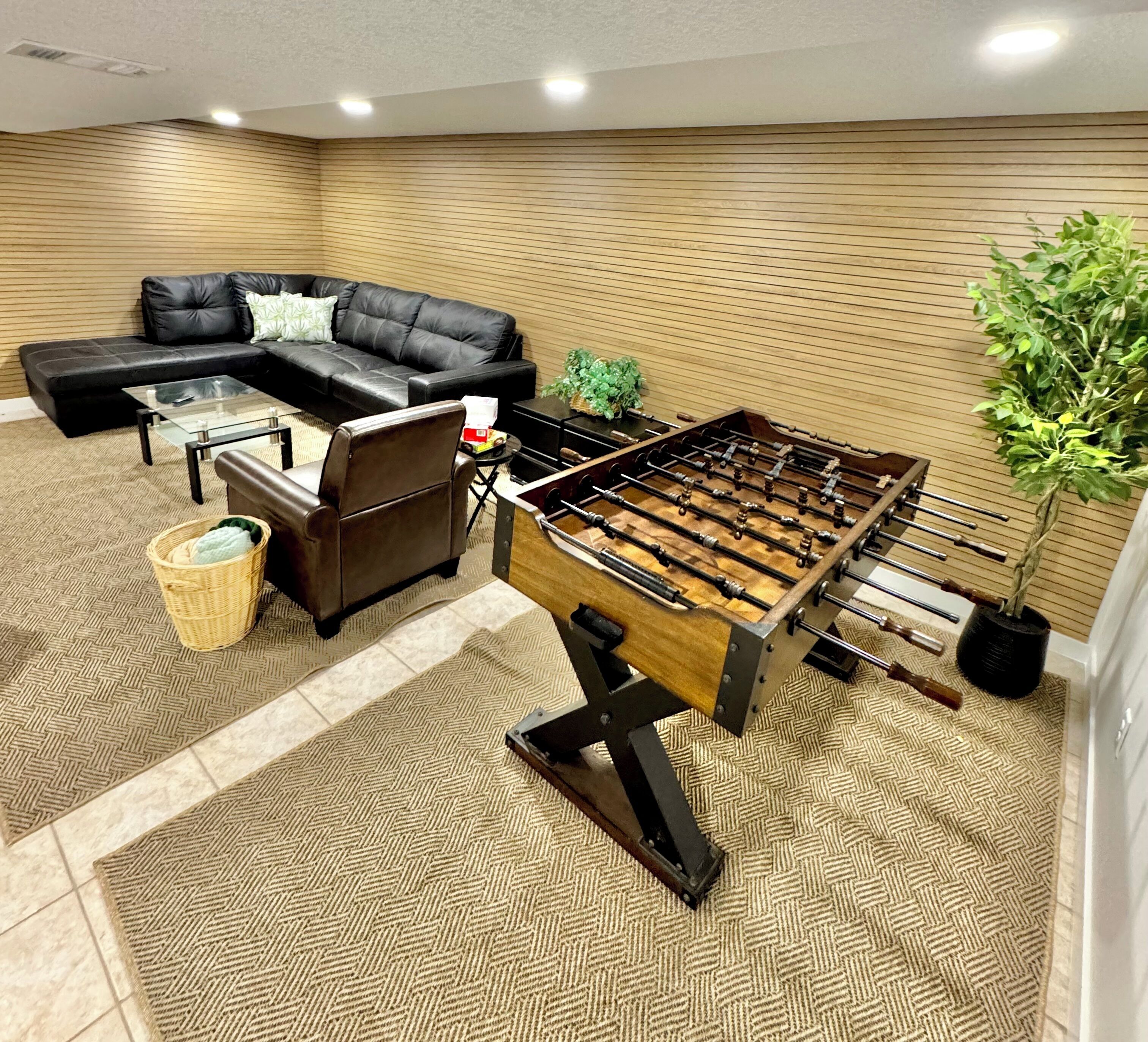 A room with a sofa, a foosball table, and a potted plant.