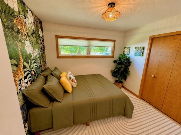 A room with a bed, a window, a door, and a wall with a tropical mural.