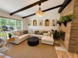 A modern living room with a sectional sofa, a round coffee table, and a brick fireplace. - Spacious, beautiful 5 Bed, 2.5 Bath modern house in Saint Paul for extended stay (Saint Paul)