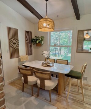 A dining area with a wooden table, four chairs, a hanging light fixture, and a window with a view of trees. - Spacious, beautiful 5 Bed, 2.5 Bath modern house in Saint Paul for extended stay (Saint Paul)