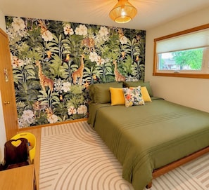 A bedroom with a green bed, a window with blinds, a wall with a jungle-themed wallpaper, and a wooden door. - Spacious, beautiful 5 Bed, 2.5 Bath modern house in Saint Paul for extended stay (Saint Paul)