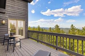 Une terrasse en bois avec une table et des chaises, une porte-fenêtre coulissante et une vue sur un paysage boisé.