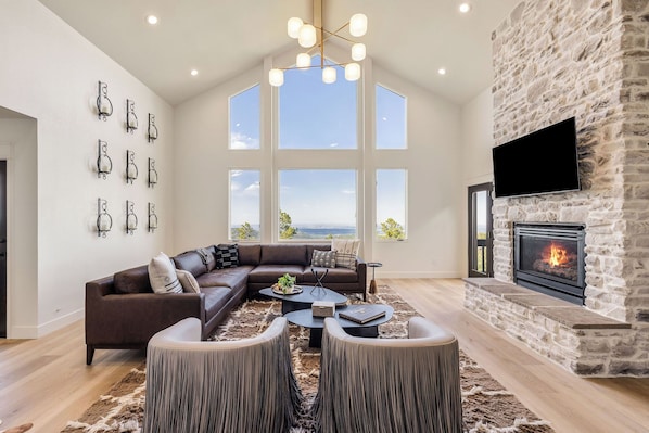 A spacious living room with a stone fireplace, a large sectional sofa, a coffee table, and a television mounted on the wall.