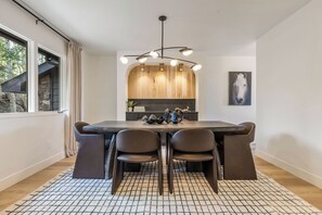 Un comedor con una mesa de madera, sillas negras, un tapete estampado, una lámpara colgante y una pared de piedra.