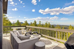 A deck with outdoor furniture, a table, and a view of a forest and mountains.