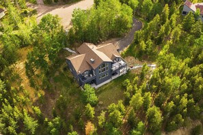 Une grande maison dotée d’une vaste terrasse, entourée d’arbres denses.