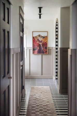 A hallway with a checkered floor, a painting on the wall, and a door on the left.
