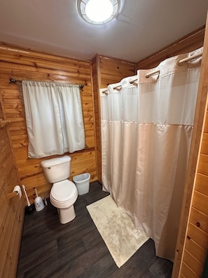Et badeværelse med træpaneler, der indeholder toilet, bidet, skraldespand og bruseforhæng.