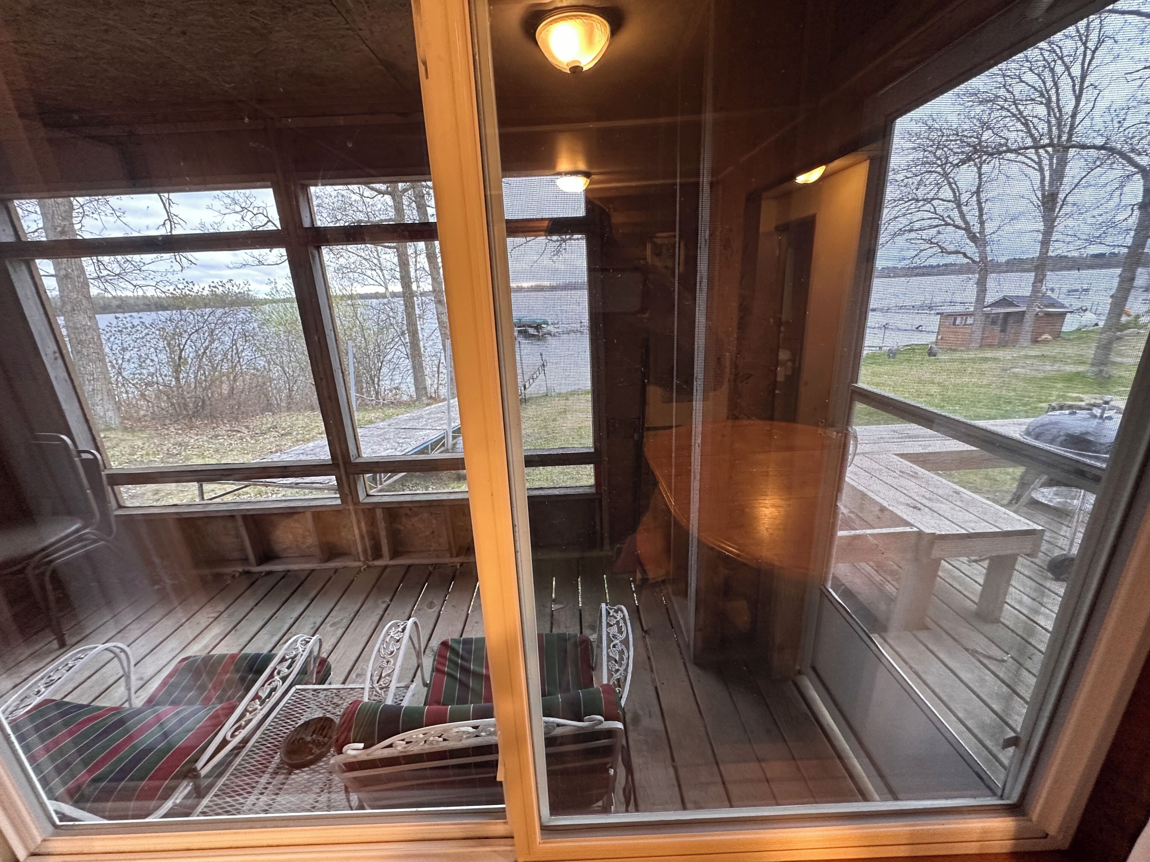 A screened porch with a view of a grassy area and trees, a wooden bench, and a table.