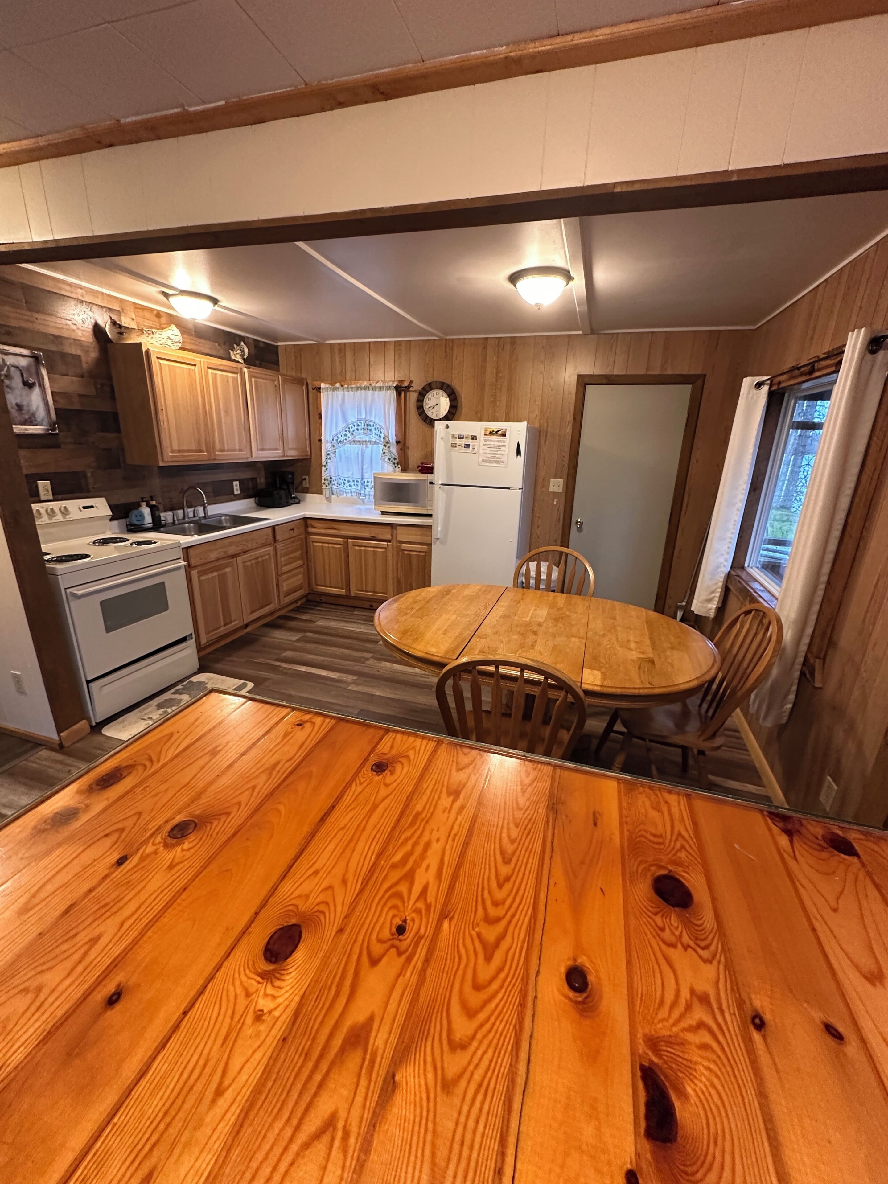A compact kitchen with wooden cabinets, a white refrigerator, a microwave, and a stove. There is a wooden dining table with chairs.