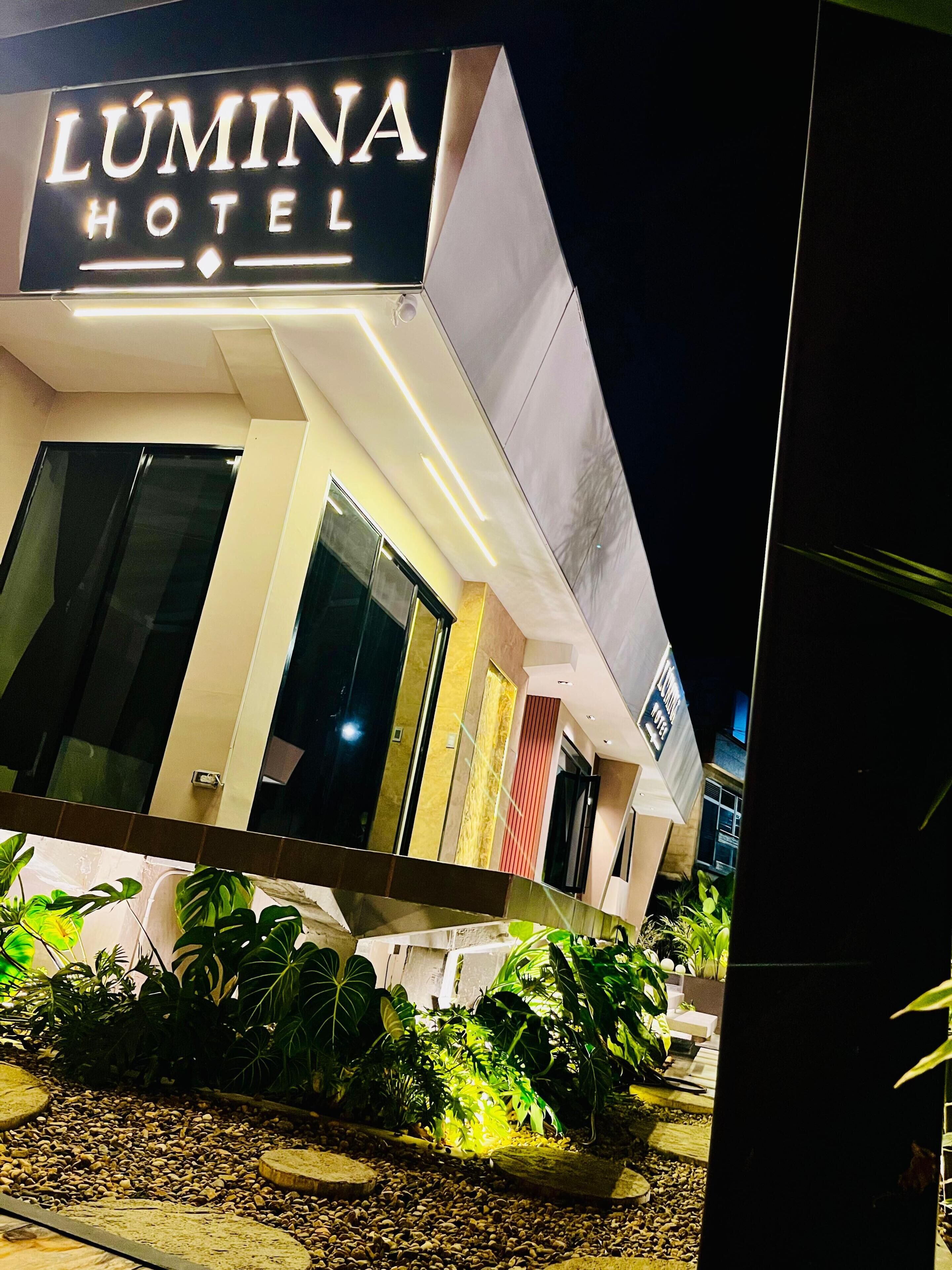A hotel named 'Lúmina Hotel' with a modern design, large windows, and outdoor plants.