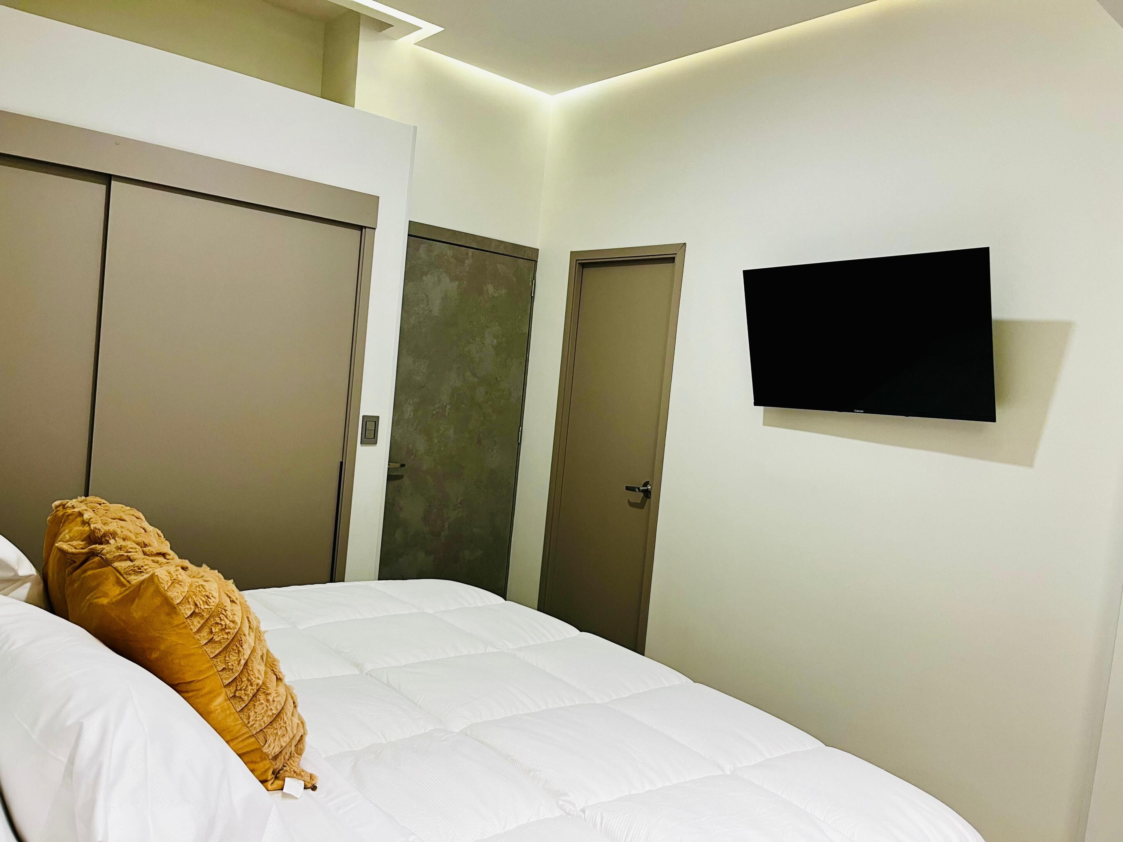 Un dormitorio con una cama, un televisor montado en la pared y dos puertas.