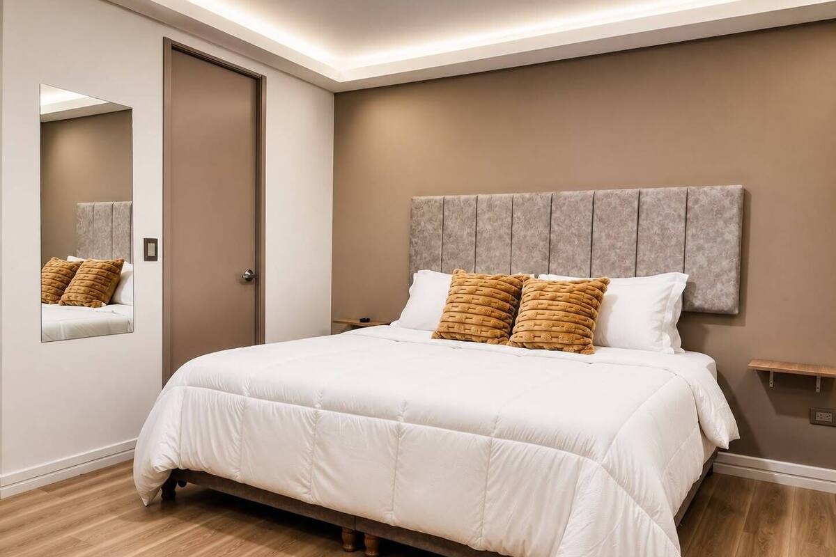 A bedroom with a bed, a headboard, a bedside table, and a mirror.