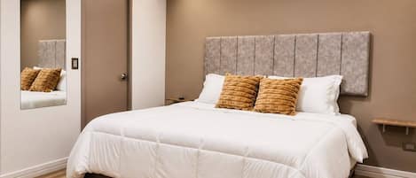 A bedroom with a bed, a headboard, a bedside table, and a mirror.