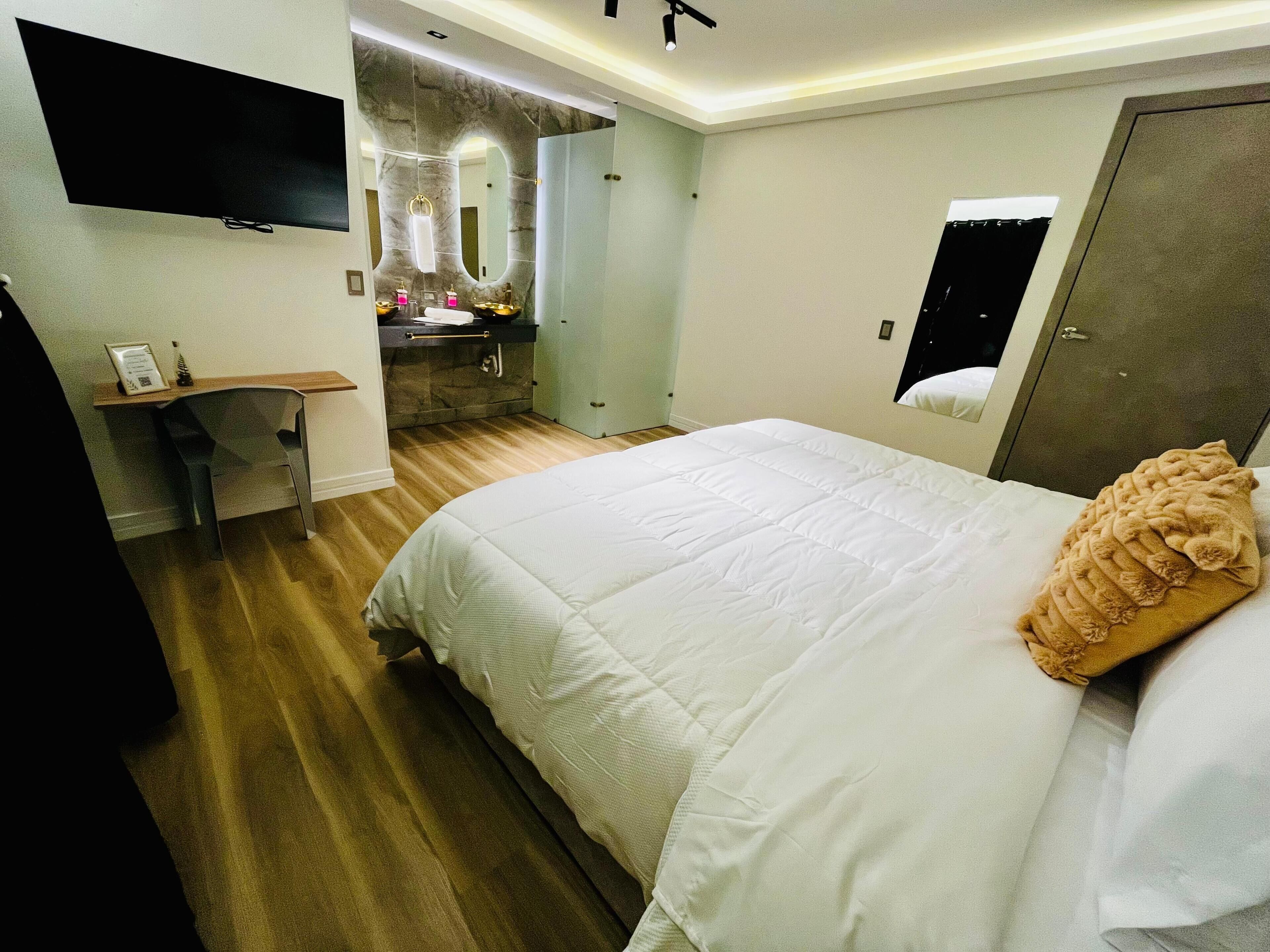 A hotel room with a bed, a desk, a mirror, and a bathroom.