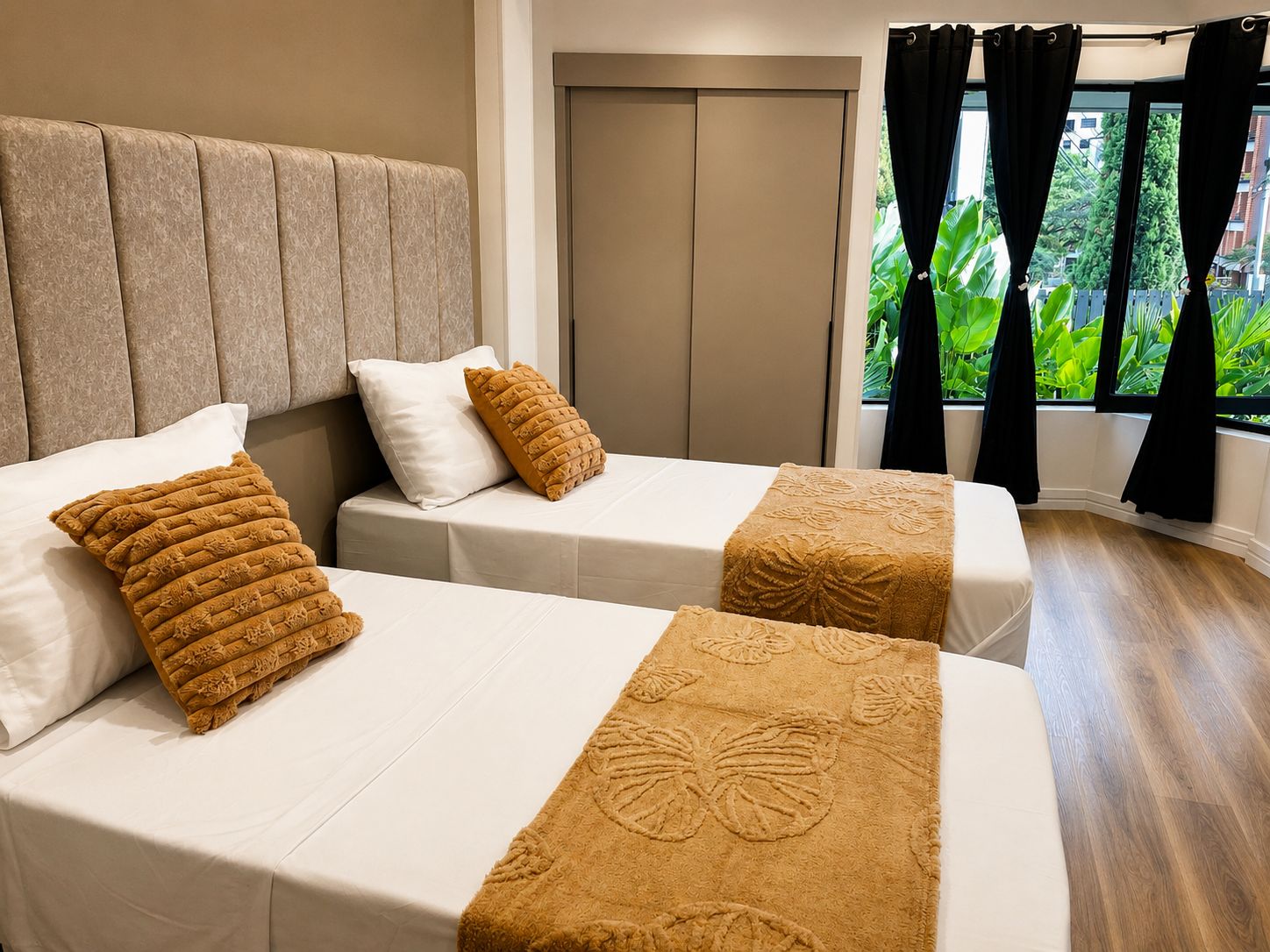 Quarto de hotel com duas camas, uma janela grande com cortinas e vista para o verde lá fora.