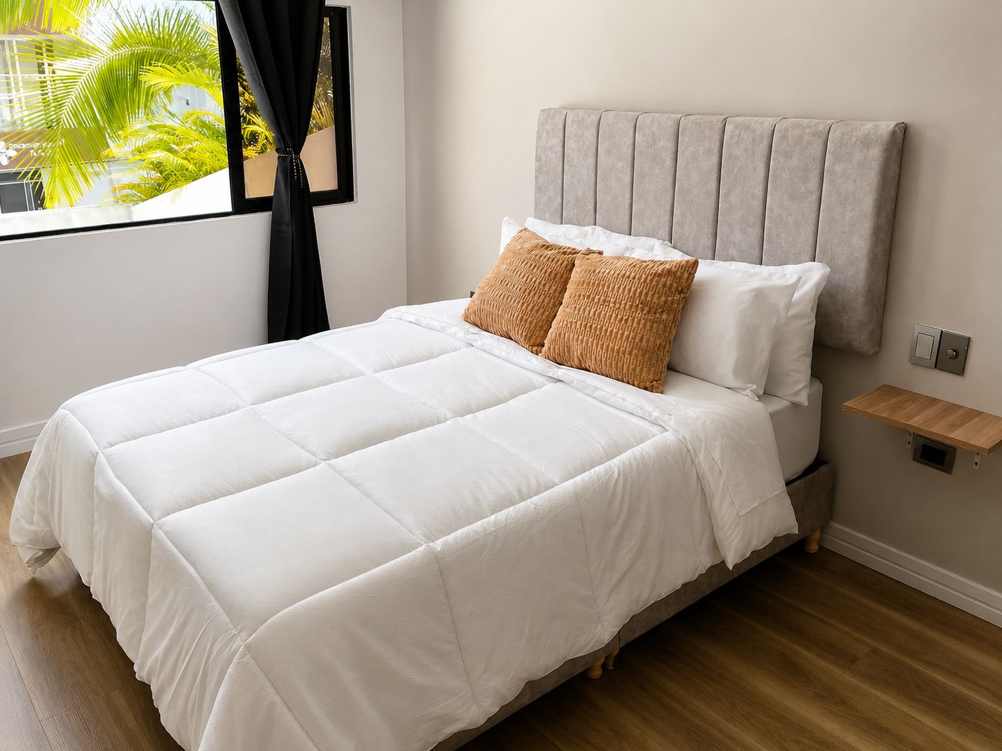 A neatly made bed with a grey headboard, white bedding, and two patterned pillows.