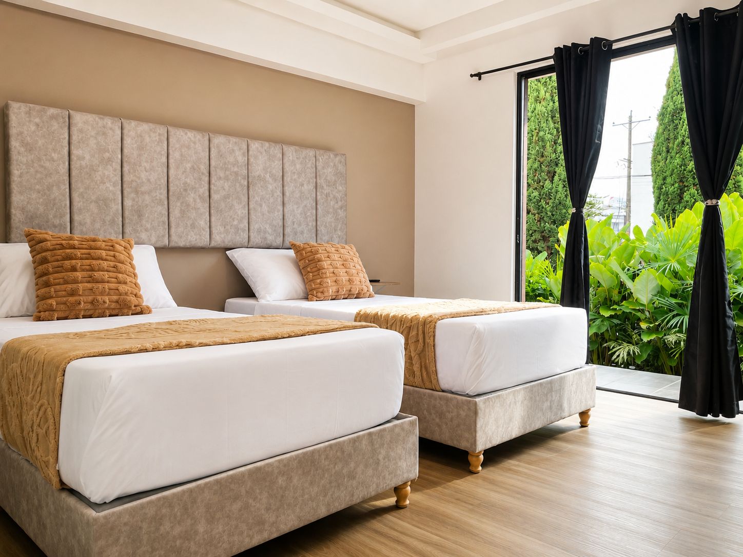 A hotel room with two beds, a large window with curtains, and a view of greenery outside.