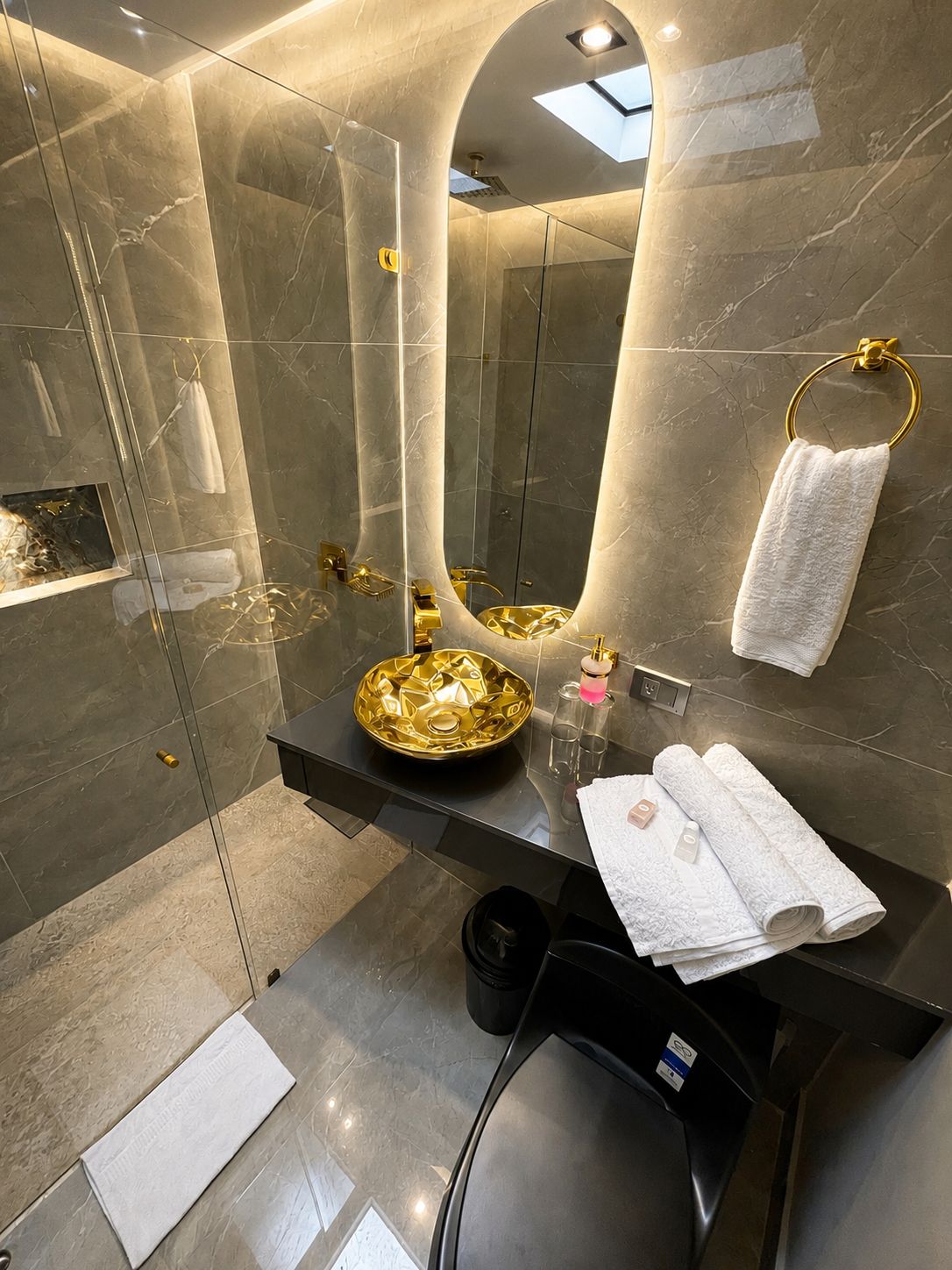 A modern bathroom with a glass-enclosed shower, a gold sink, and a large mirror.