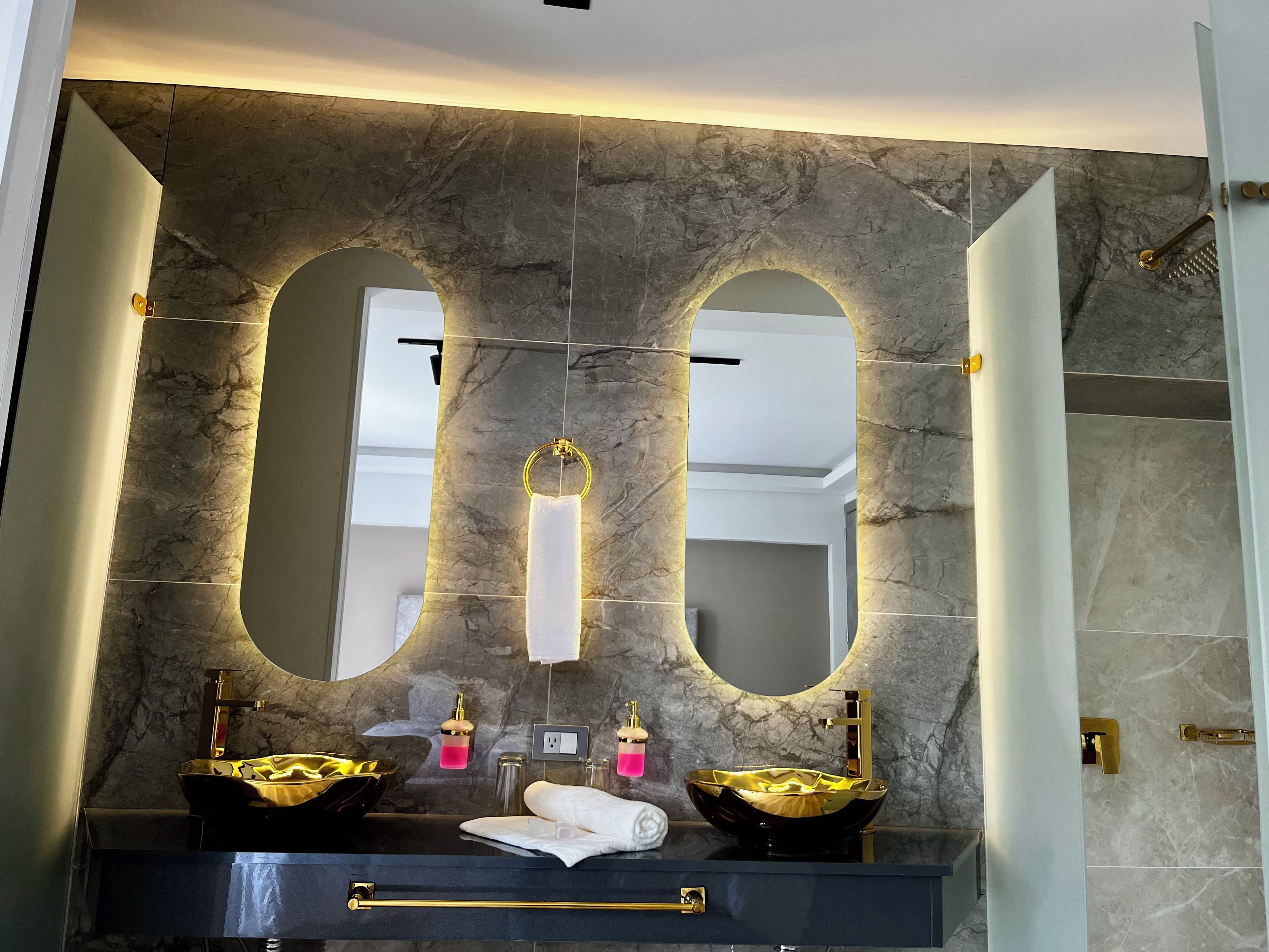 A bathroom with a marble wall, two sinks with gold fixtures, and a large mirror.