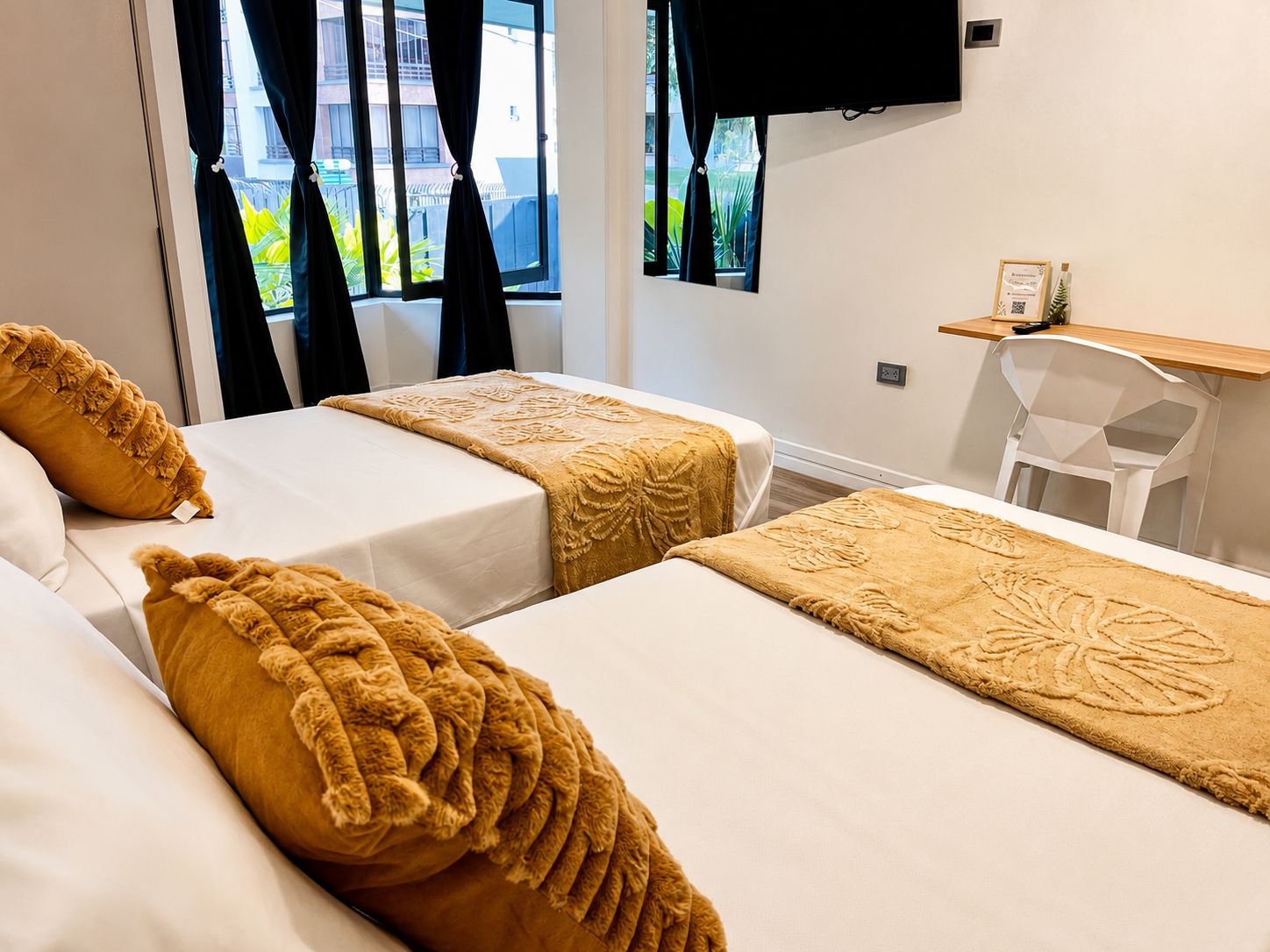 A hotel room with two beds, a TV mounted on the wall, a desk, and a chair.