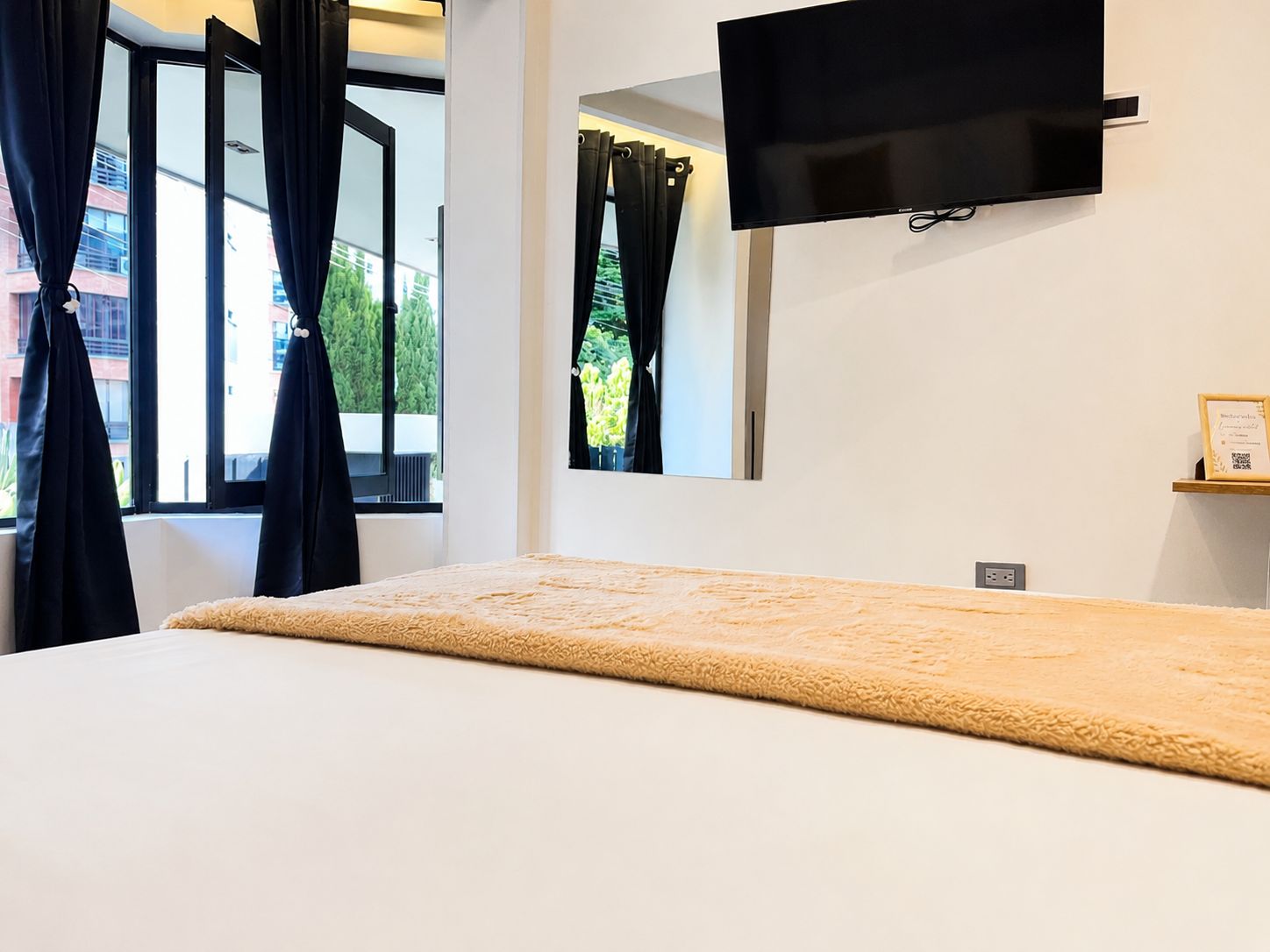 A hotel room with a bed, a TV mounted on the wall, and a window with curtains.