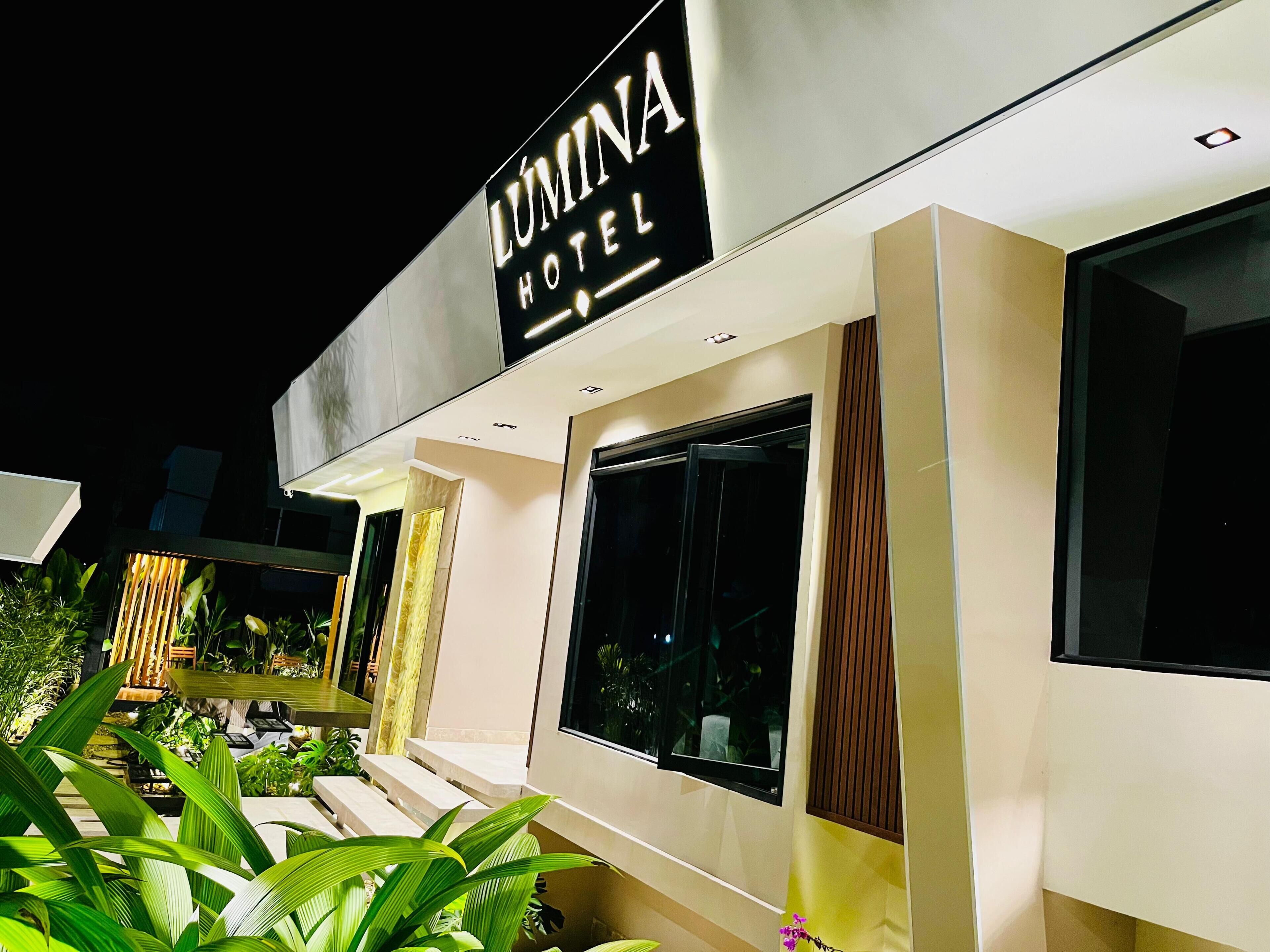 A modern hotel exterior with a prominent sign, large windows, and a well-maintained outdoor area with plants.