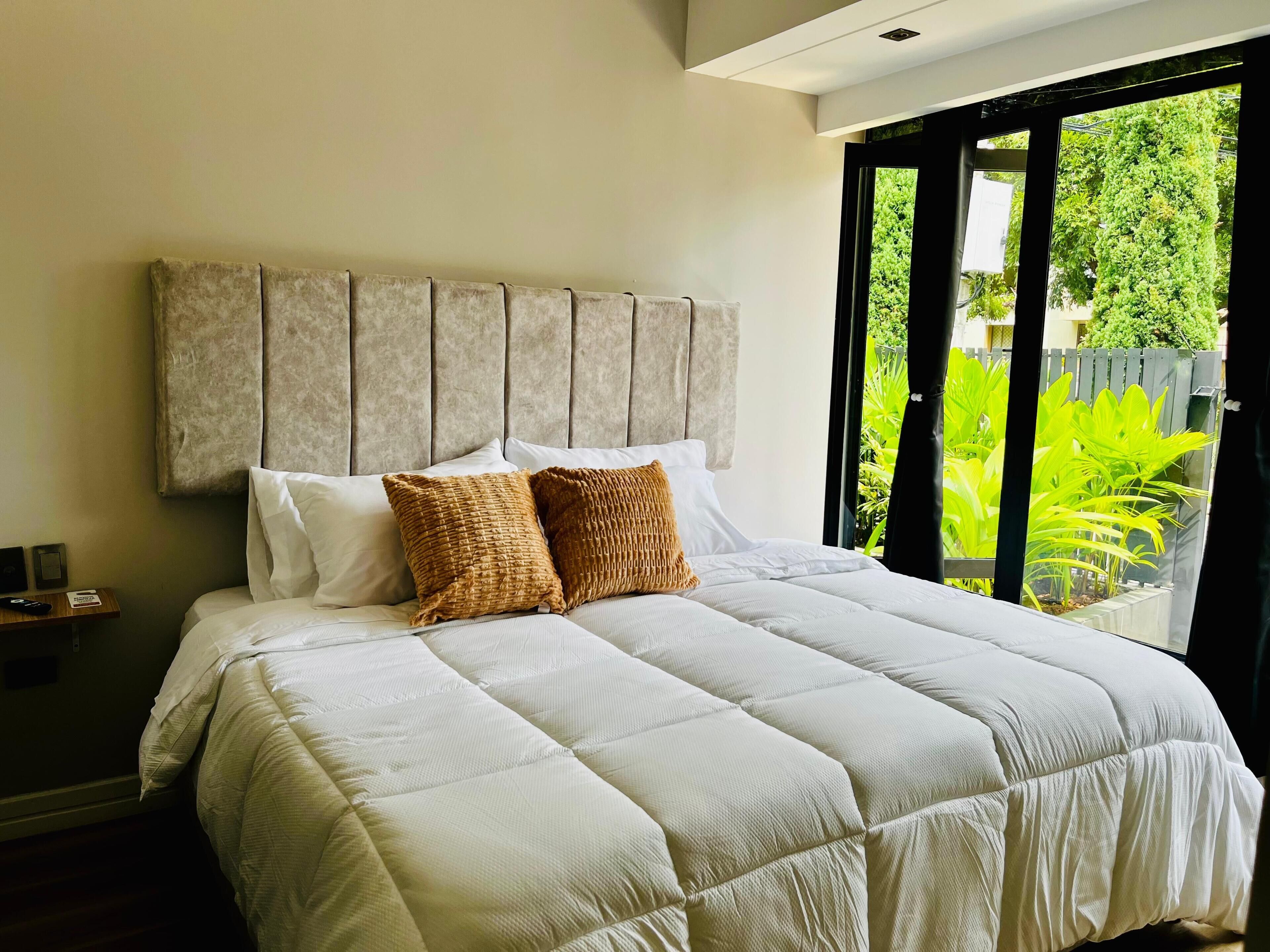 A bed with a headboard, pillows, and a view of greenery outside.
