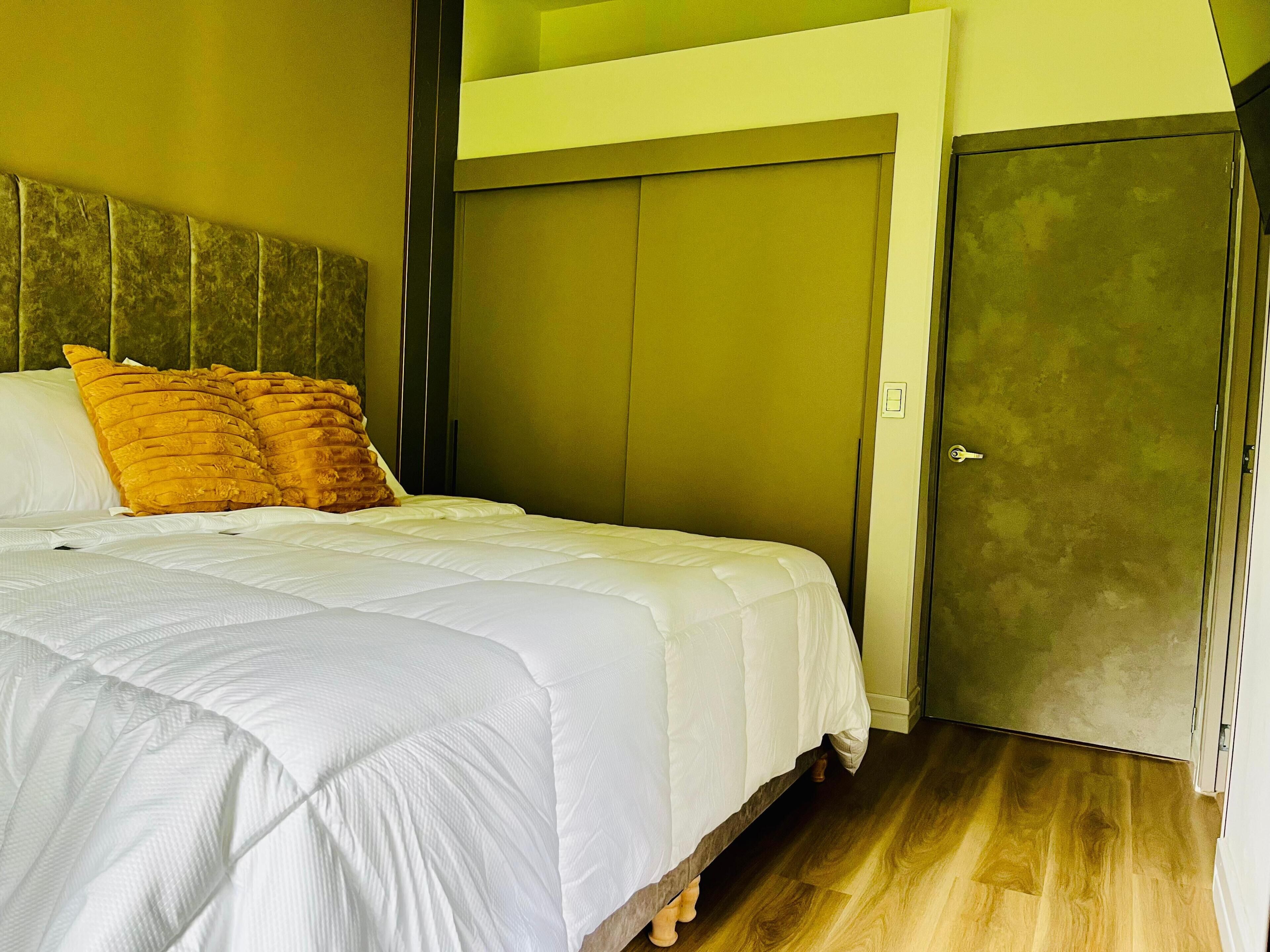 A bedroom with a bed, pillows, a wardrobe, and a door.