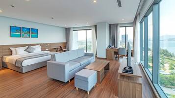 A modern hotel room with a bed, sofa, desk, and large windows offering a city view.