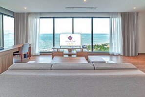 A modern hotel room with a large window, a flat-screen TV, a wooden desk, and a sofa.