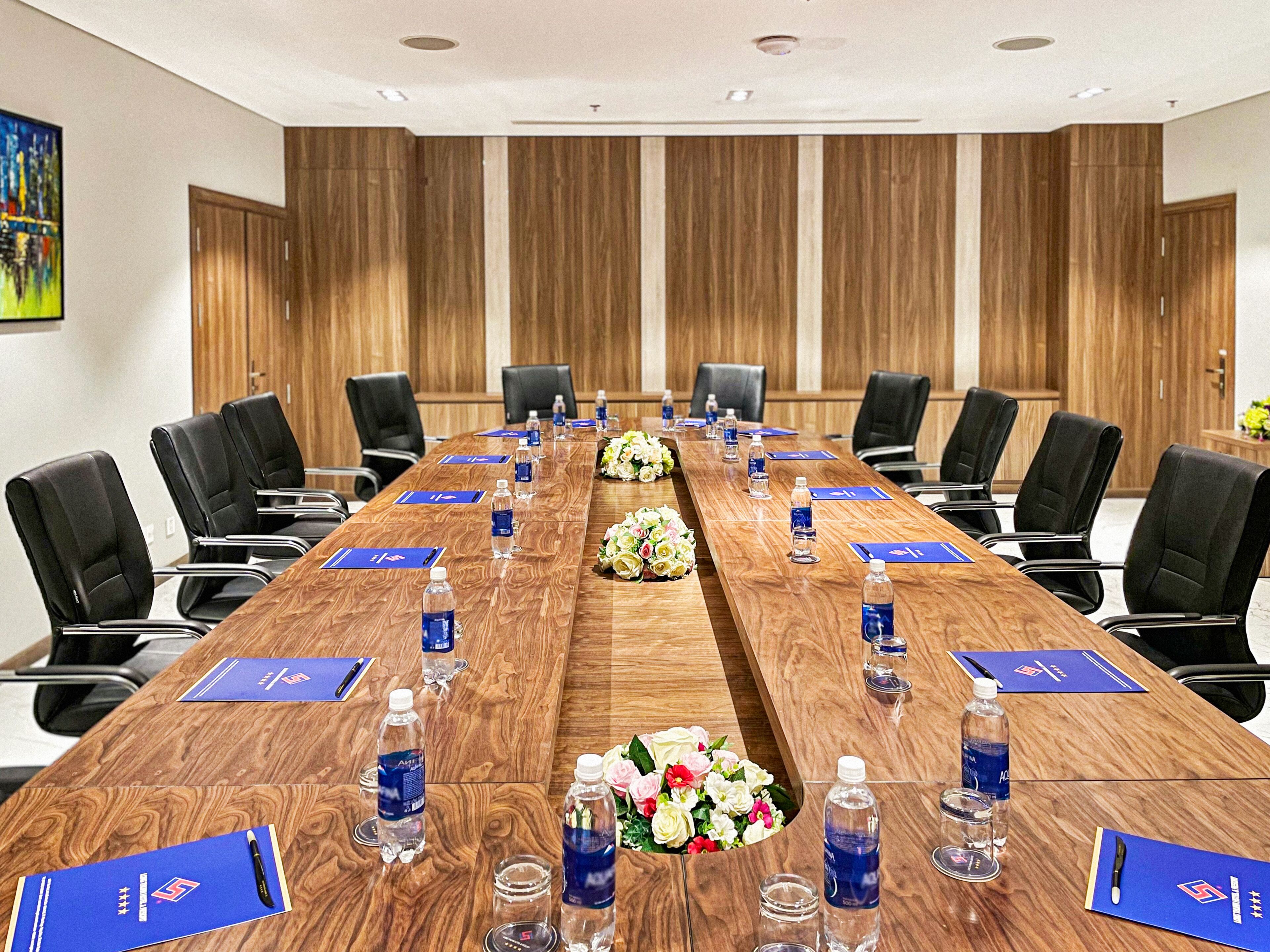 A conference room with a long wooden table, black chairs, water bottles, and blue nameplates.