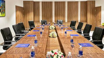 A conference room with a long wooden table, black chairs, water bottles, and blue nameplates.