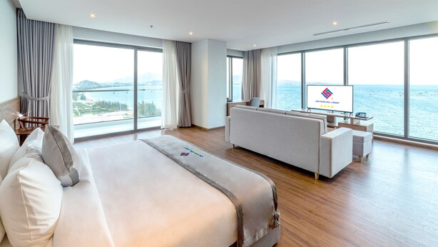 A modern hotel room with a large bed, a sofa, a TV, and a view of the sea. - Long Thuan Hotel & Resort (Dong Hai)