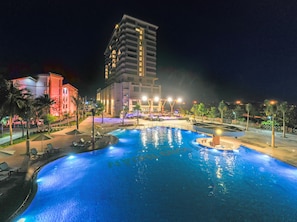 A nighttime swimming pool area with a large building in the background.