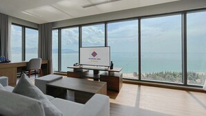 A modern hotel room with a large window, a desk with a computer, and a television displaying the hotel's logo. - Long Thuan Hotel & Resort (Dong Hai)
