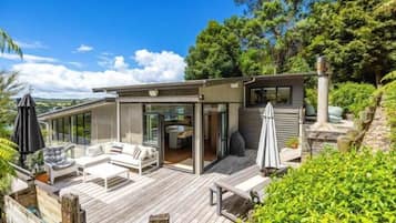 A modern house with a deck, outdoor seating, and a view of the surrounding greenery.