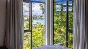 A room with large windows offering a view of a lake and greenery. - Huruhi Bay Retreat by Waiheke Pure - Views, stylish, spacious and central (Waiheke Island)