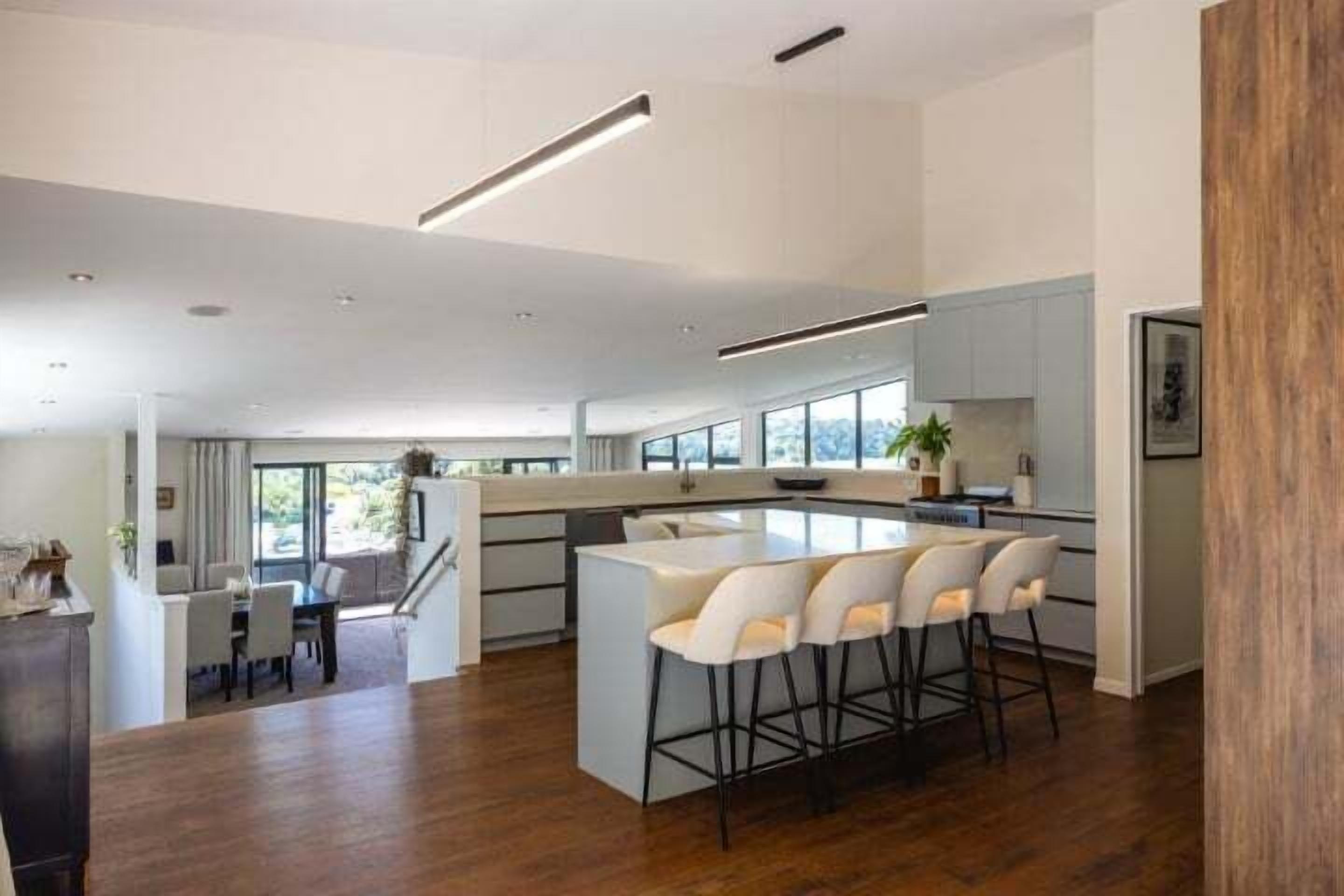 A modern kitchen with a central island, bar stools, and a dining area with a table and chairs.