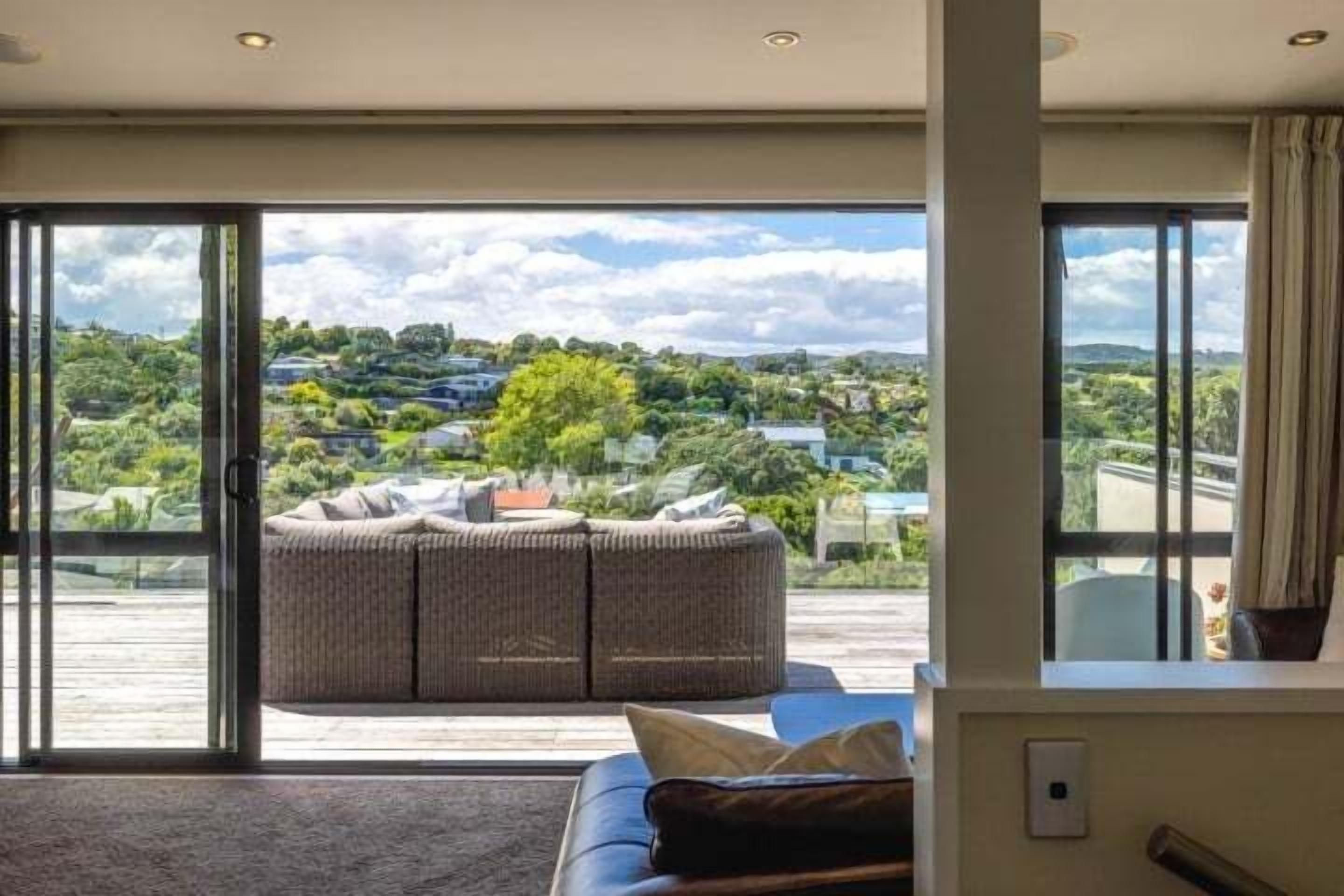 A room with a large sliding glass door leading to a balcony, a wicker sofa, and a view of a green landscape.