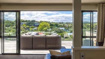 A room with a large sliding glass door leading to a balcony, a wicker sofa, and a view of a green landscape.