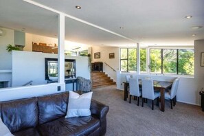 Un salon moderne avec un canapé en cuir, un coin repas comprenant une table et des chaises, et un escalier menant à un niveau supérieur.