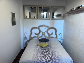 Una camera da letto con un letto, due lampade ai comodini, uno specchio sopra il letto e una mensola con dei libri.