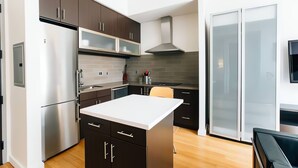 A modern kitchen with dark cabinets, a stainless steel refrigerator, a white countertop island, and a built-in microwave. - Central 1-bedroom condo in vibrant San Francisco Downtown (San Francisco)