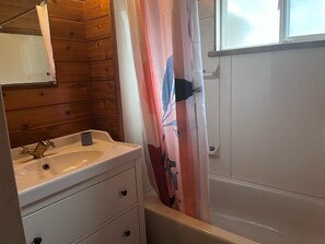 A bathroom with a wooden wall, a sink with a faucet, a shower curtain, and a bathtub.