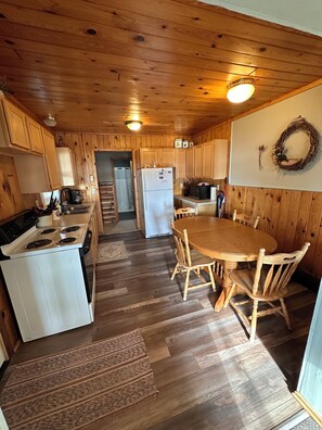 A wooden cabin interior with a kitchen, dining area, and a staircase leading to an upper level. - Cabin #2, quaint 3-Bed with AC on Lake Andrusia on the Cass Lake chain (Cass Lake)
