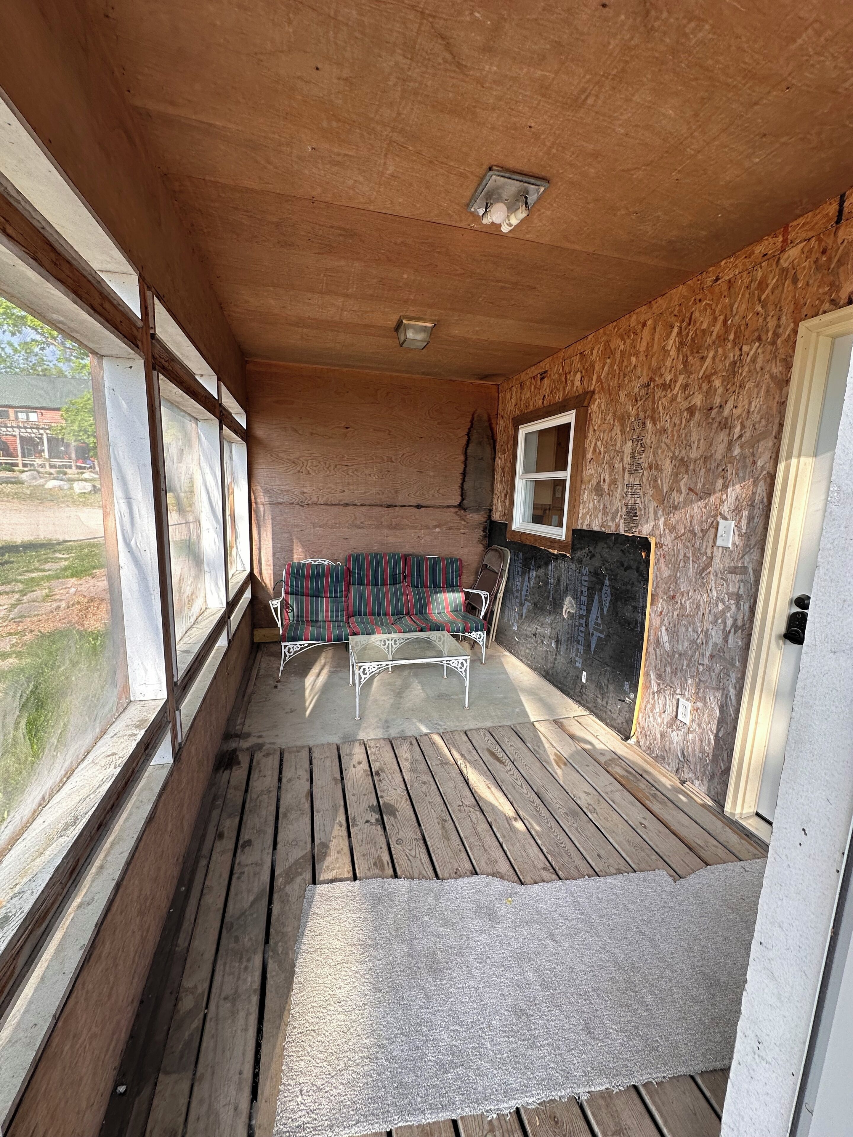 A covered porch with a wooden floor, a metal table, and striped outdoor furniture.