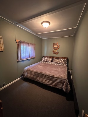 A bedroom with a bed, a window with curtains, a ceiling light, and a wall decoration. - Cabin #2, quaint 3-Bed with AC on Lake Andrusia on the Cass Lake chain (Cass Lake)
