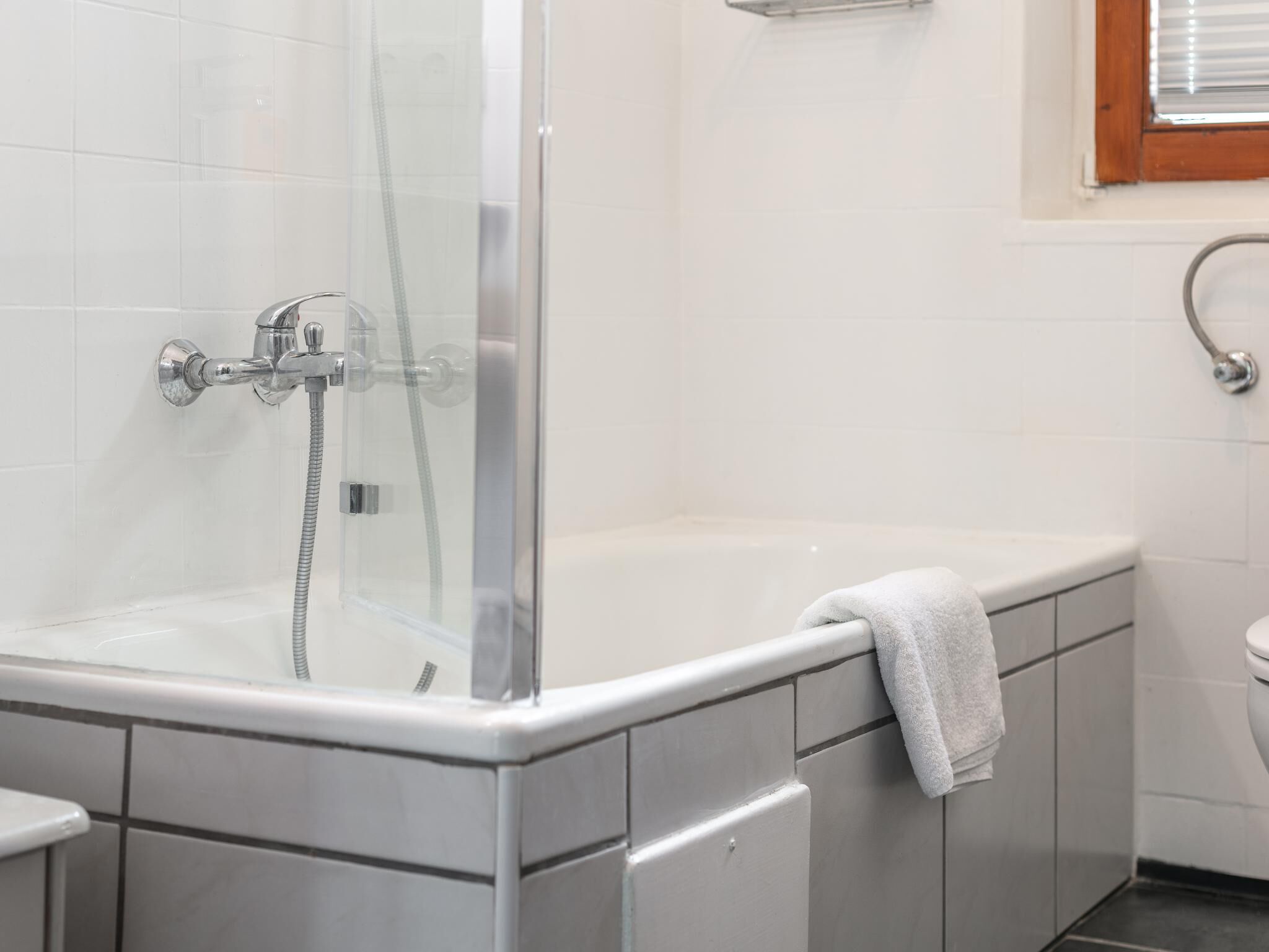 A shower enclosure with a glass door, a bathtub with a towel, and a toilet in a bathroom with white tiled walls.