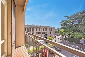 A balcony with a view of a street, a building with a tiled roof, and a tree.